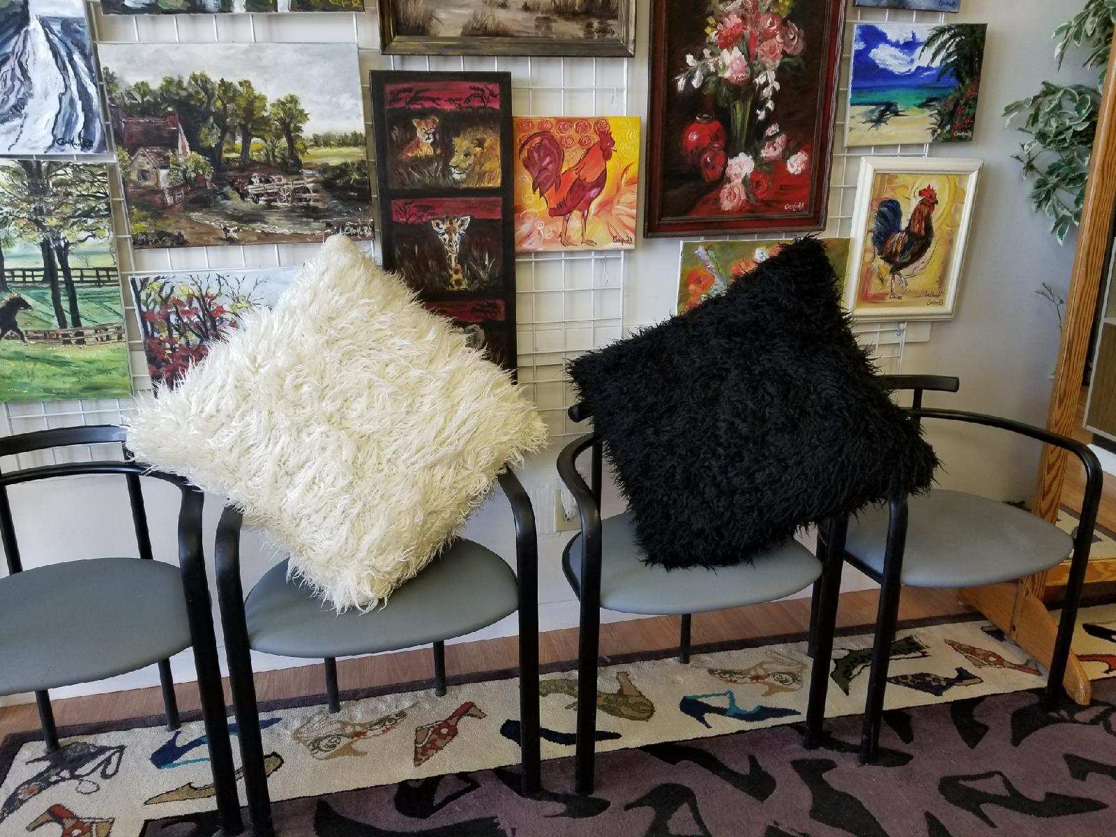 Two modern chairs with white and black pillows in an art-filled gallery corner