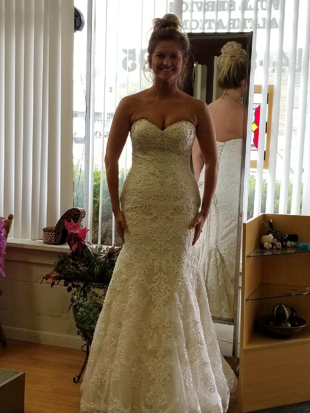Woman in a strapless ivory lace gown standing indoors by a window.