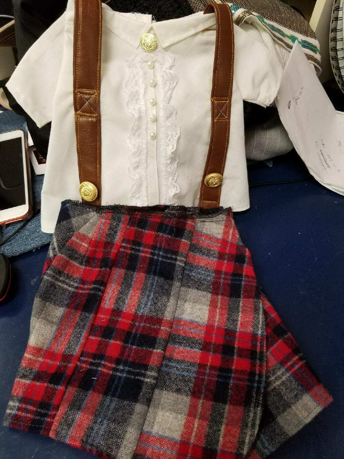 White shirt with brown suspenders and a red-and-black plaid skirt on a mannequin.
