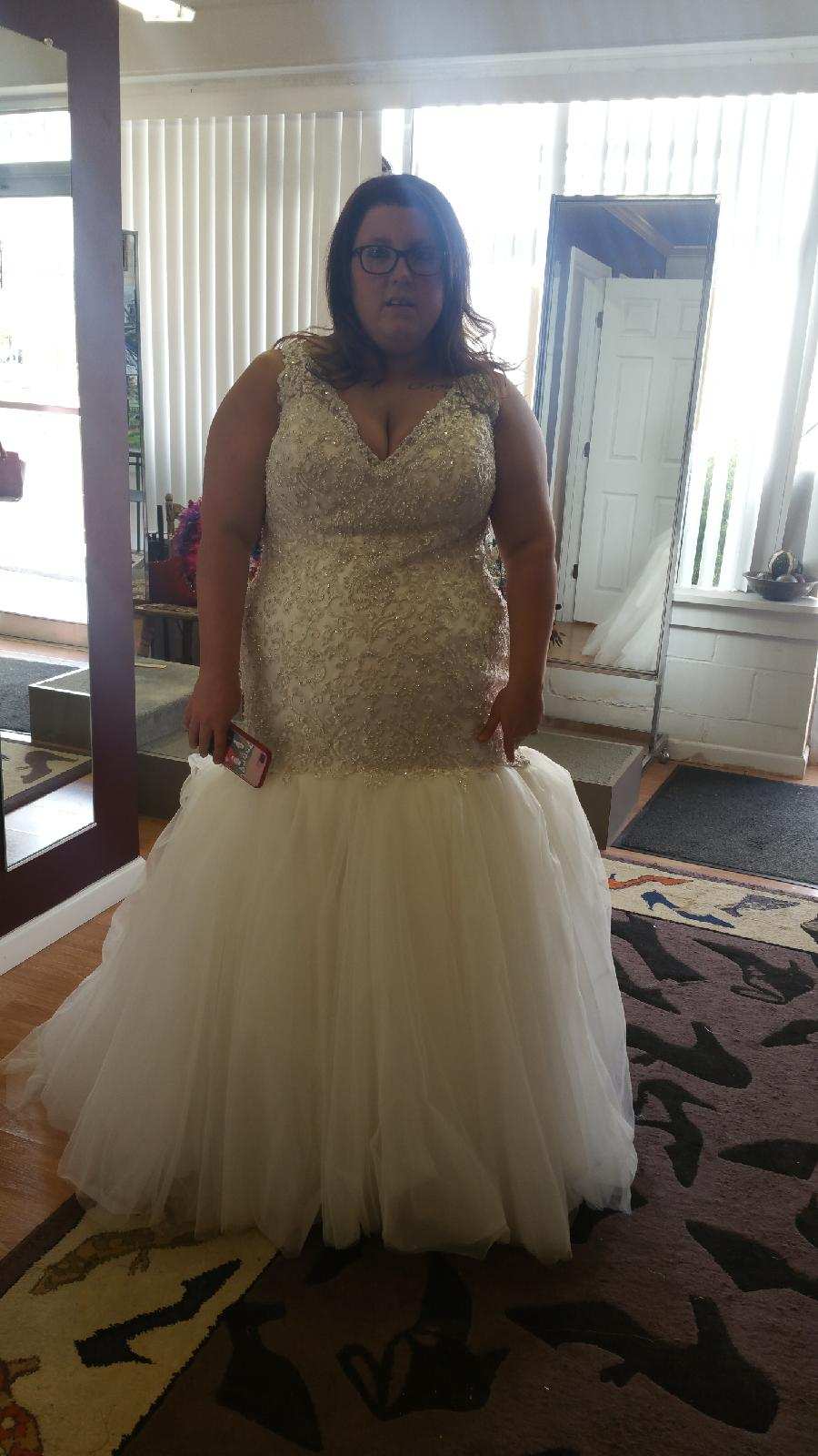 Person standing indoors in a gold top and cream tulle skirt, in front of a mirror and window blinds.