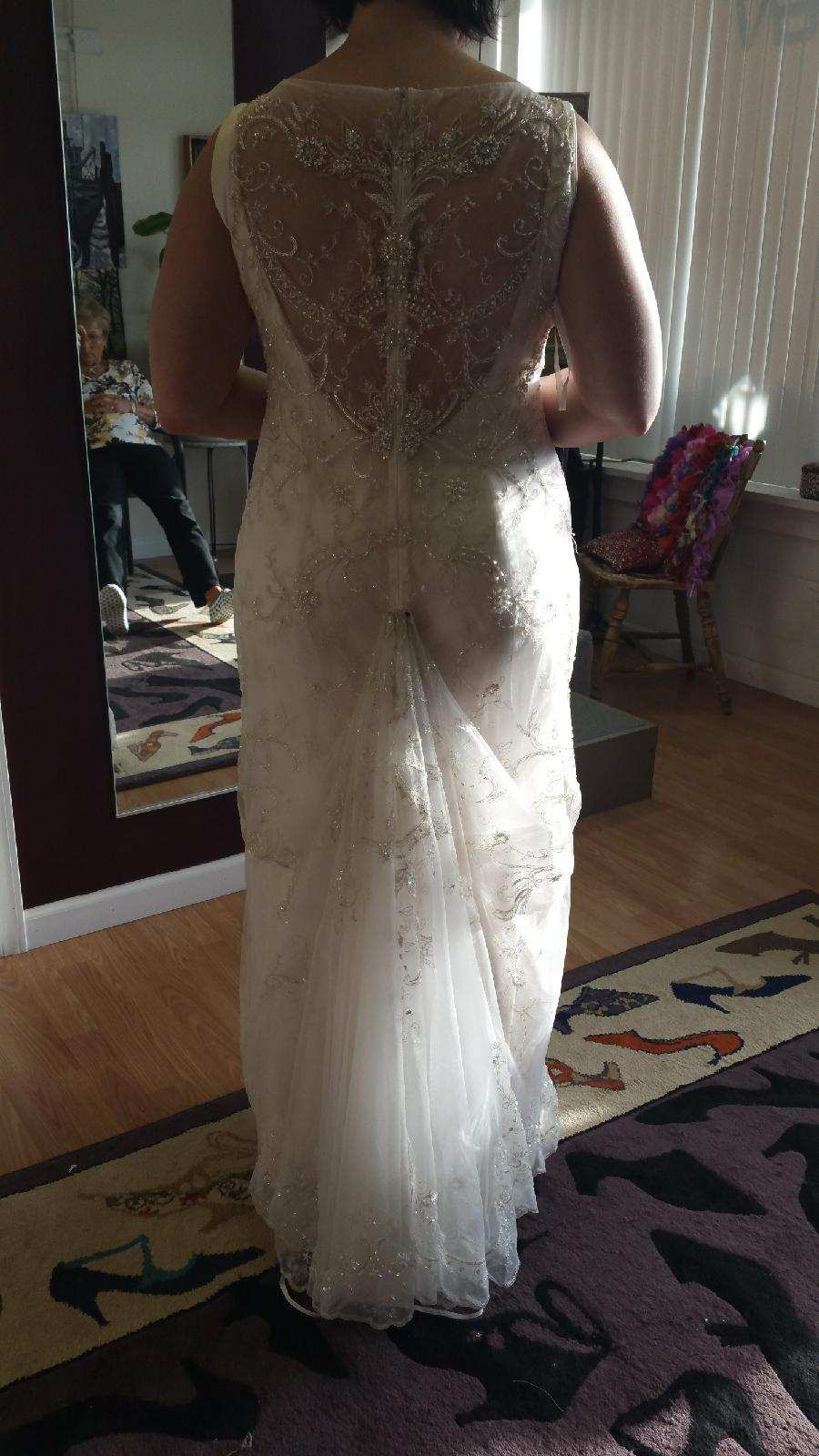 Woman in a white lace wedding dress viewed from behind, standing indoors near a mirror.
