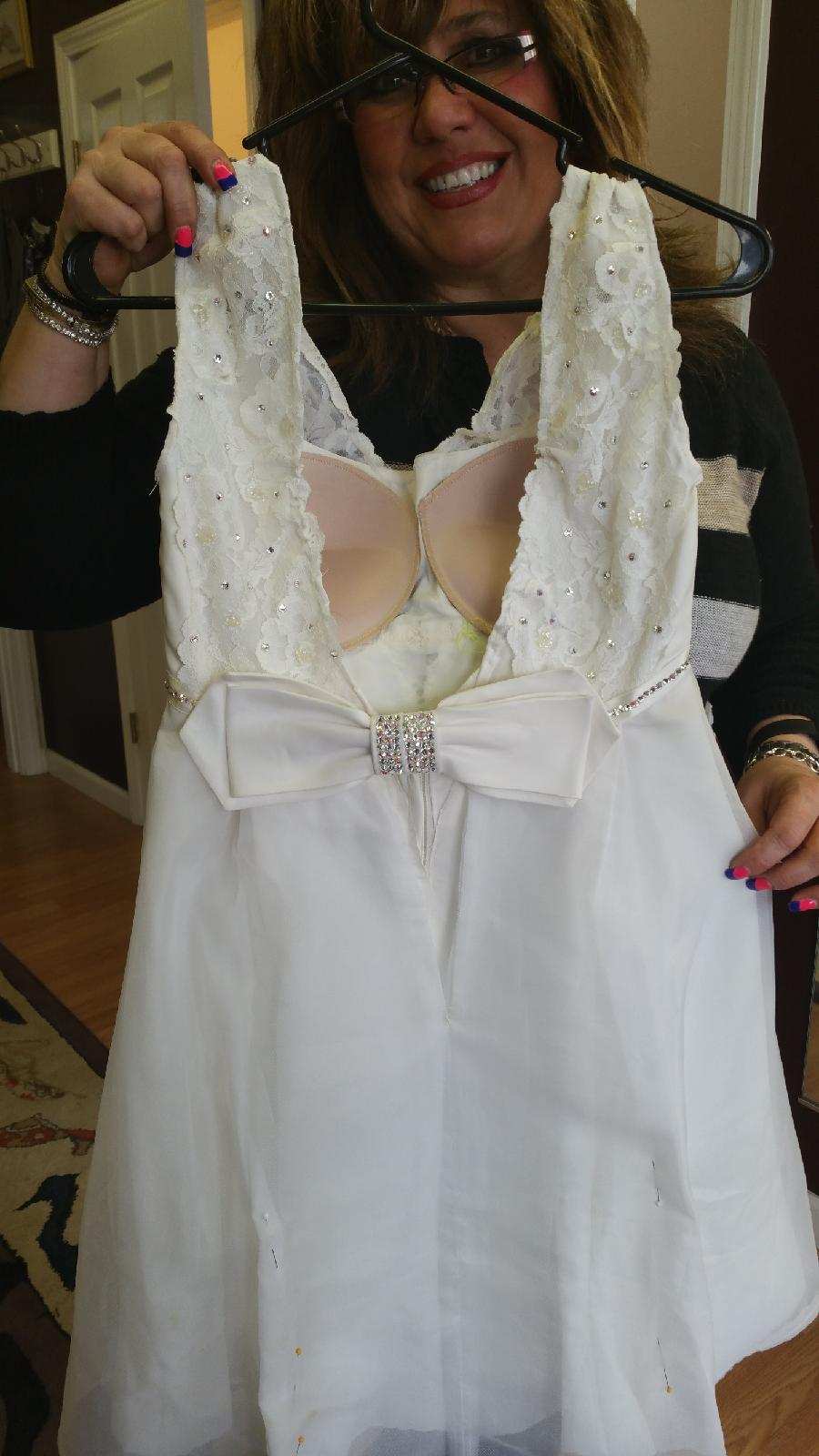 White sleeveless dress on a hanger, featuring a bow and beaded bodice, held up by a smiling person.