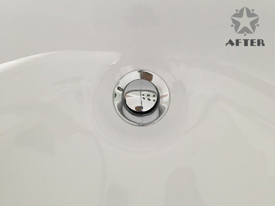 Chrome bathroom sink drain with a small toy face reflected in it, on a white basin.