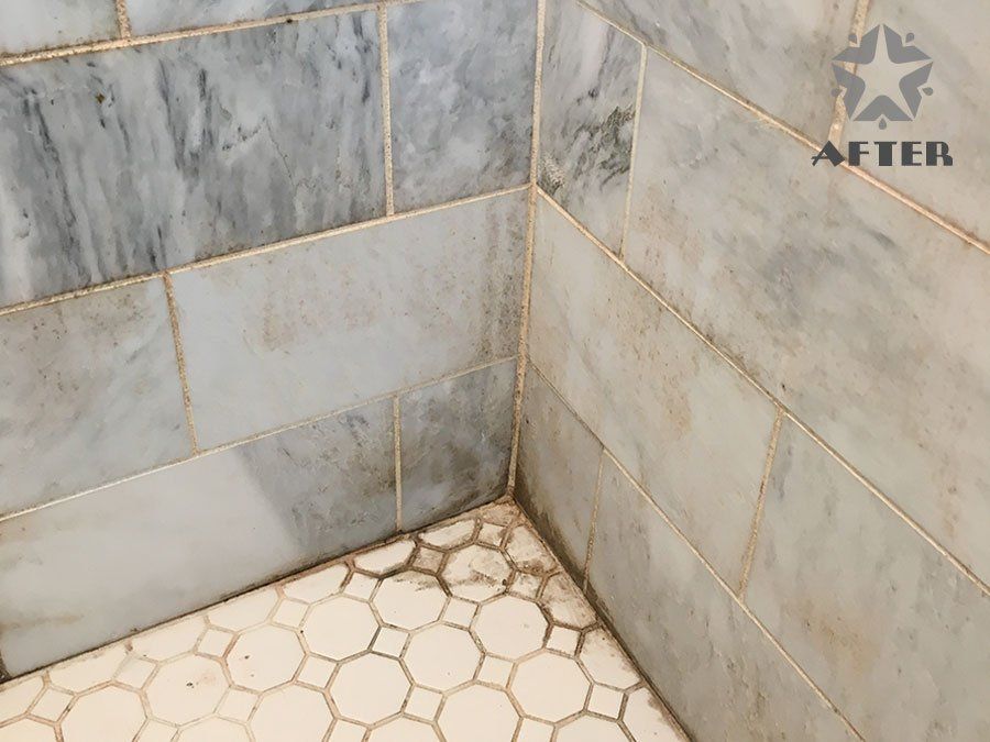 Corner of a tiled shower with gray marble walls and beige hexagon floor tiles.