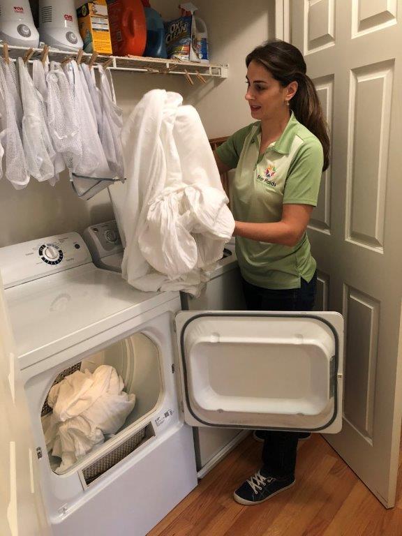 Woman unloading white laundry from a dryer in a small laundry room