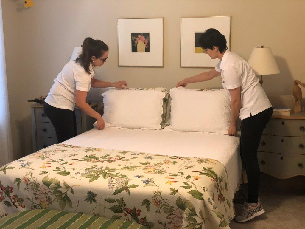 Two people making a bed with white linens and a floral duvet in a bedroom