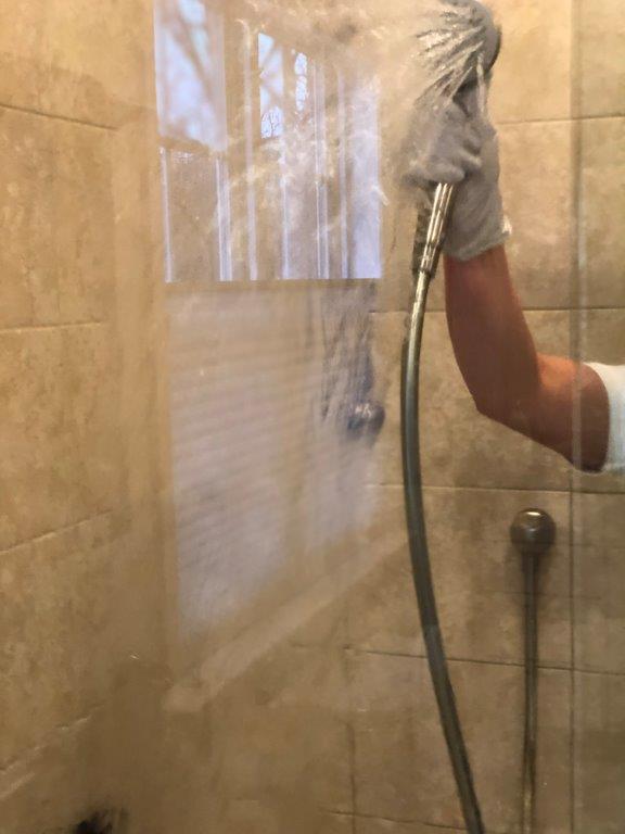 Person spraying a shower wall with a handheld showerhead in a tiled bathroom