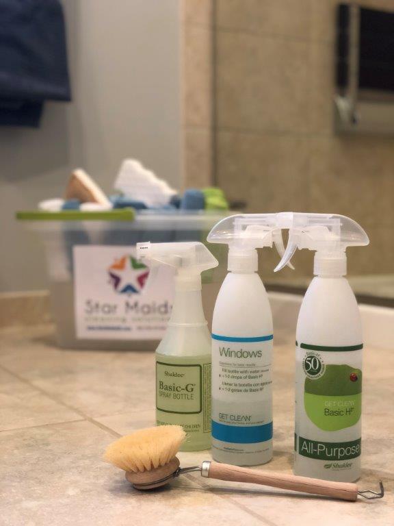 Cleaning supplies on a tiled bathroom floor, including spray bottles, a sponge, and a bucket.