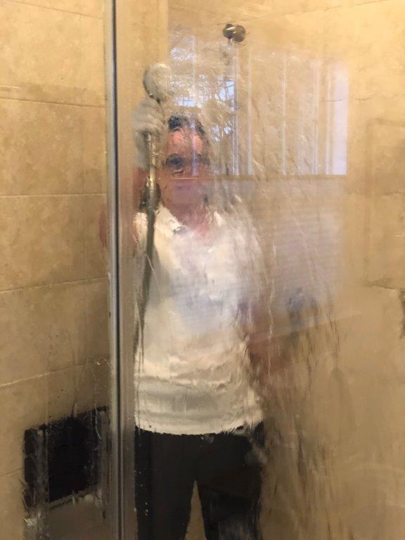 Person taking a shower behind a foggy glass door in a tiled bathroom.