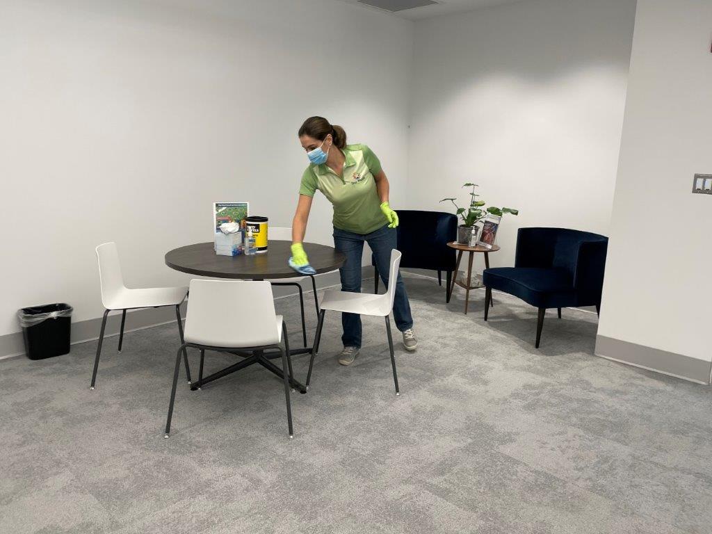 Person cleaning a round table in a small office lounge with chairs and a blue armchair.