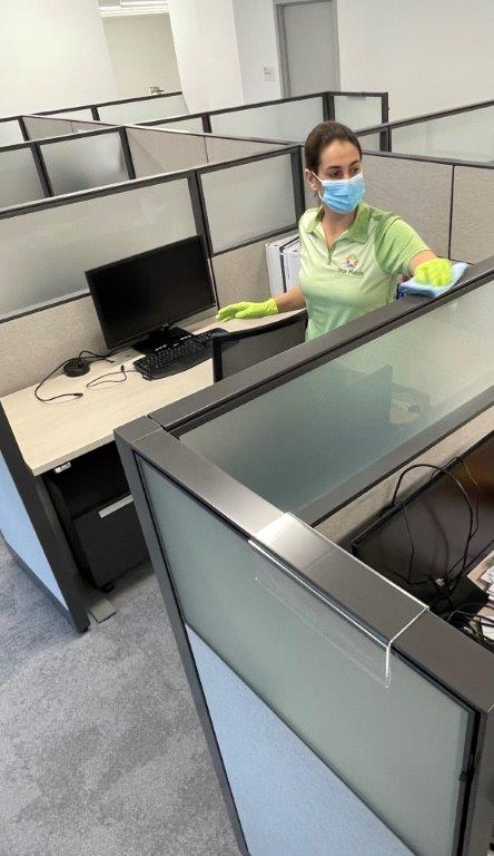 Office worker wearing a mask and gloves sits at a cubicle in an empty office.