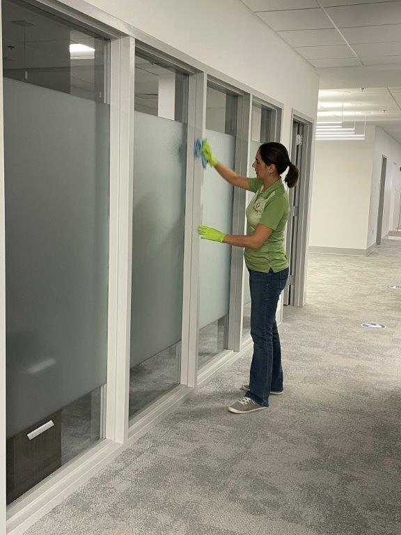 Person cleaning office glass doors with a green cloth in a hallway