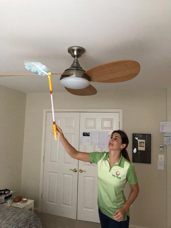 Woman dusting a ceiling fan with a long duster in a room with double doors.