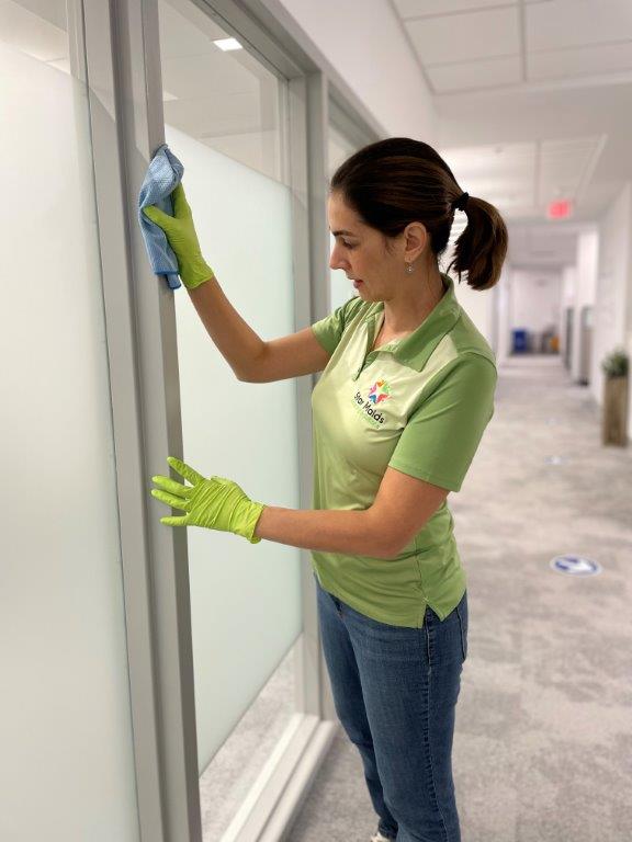 Worker cleaning glass hallway windows with spray bottle and cloth in a bright office corridor