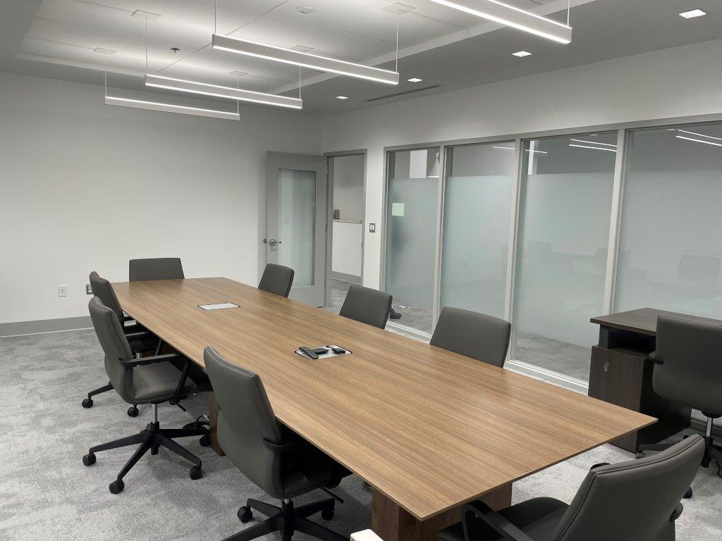 Modern conference room with a long wooden table, black chairs, and glass walls.
