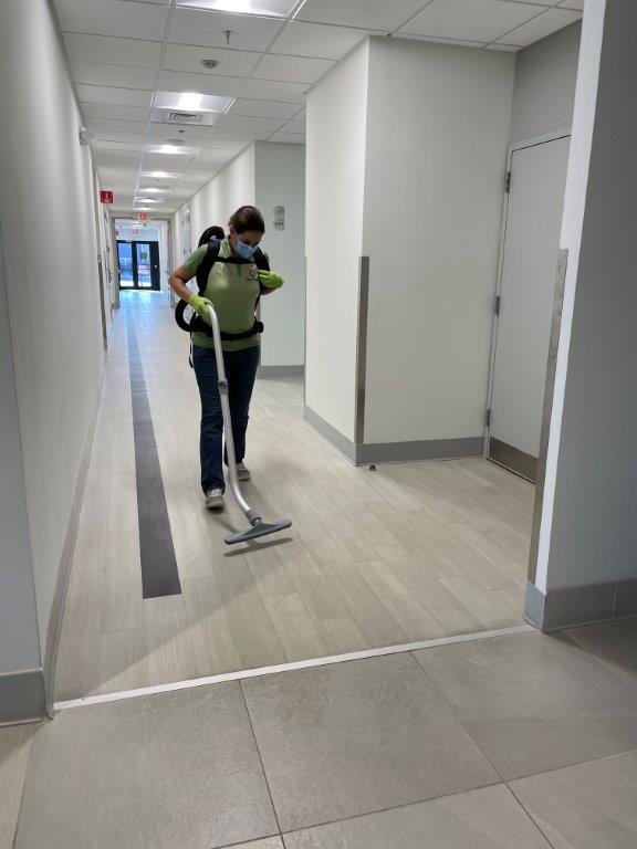 Person vacuuming a bright hallway with a backpack vacuum and floor nozzle