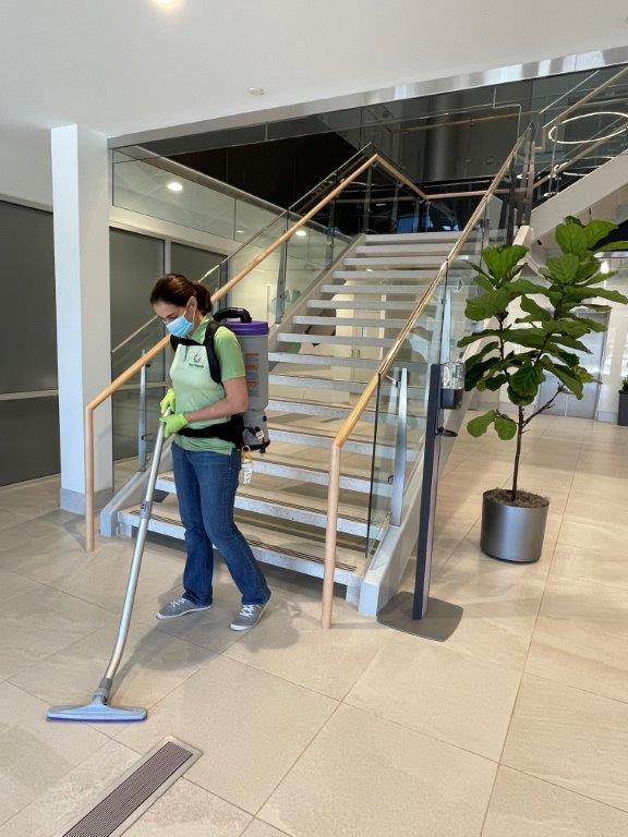 Person mopping a lobby floor near a staircase and potted plant