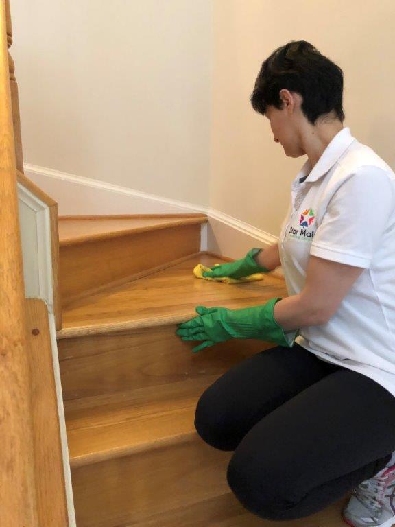 Person kneeling while cleaning wooden stairs with a cloth and green gloves