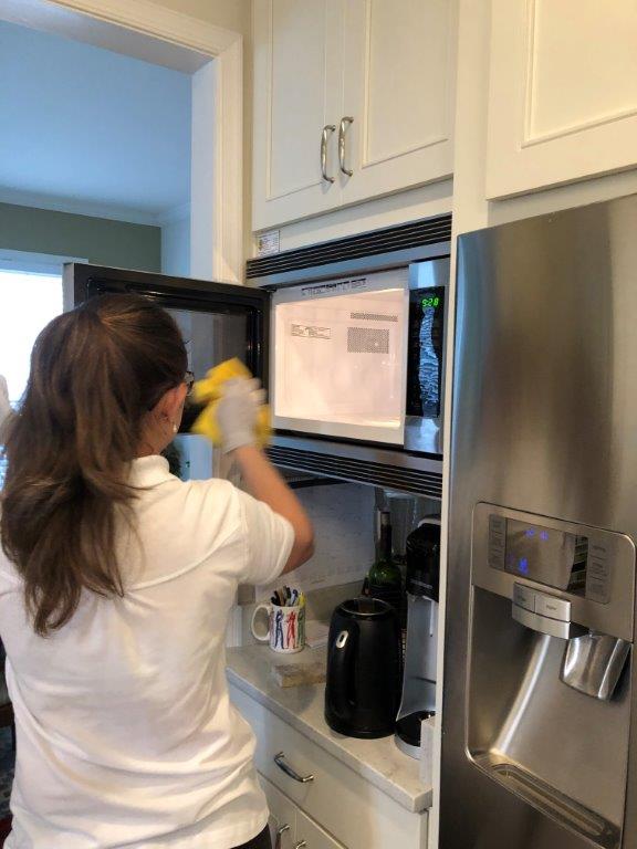 Person placing an item in a microwave in a kitchen, beside a stainless steel refrigerator.