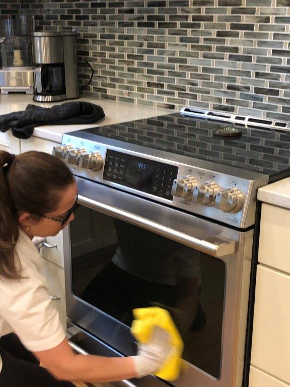 Person wiping the front of a stainless steel oven in a kitchen