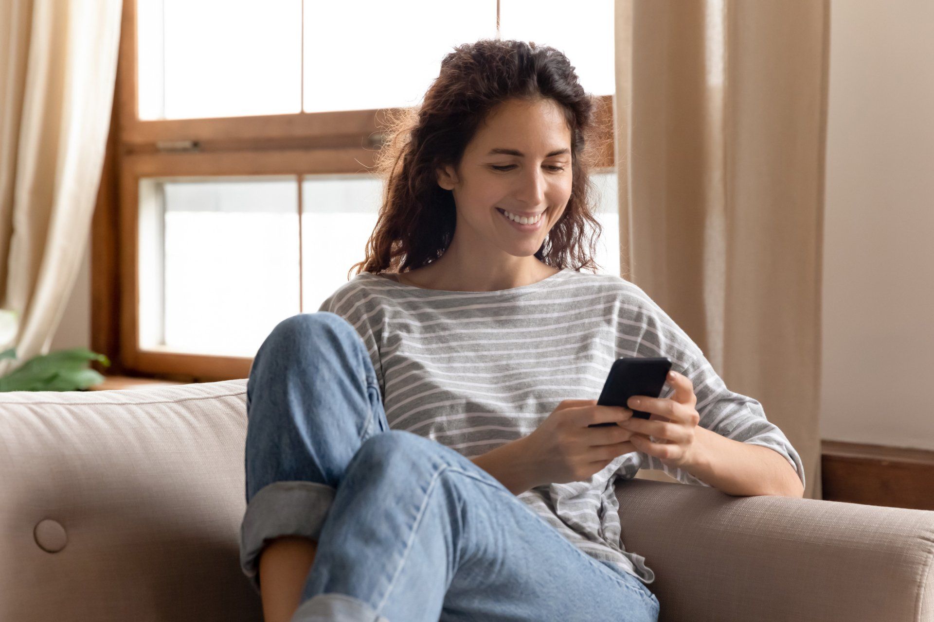 Happy Woman - Olney, Maryland - Star Maids Cleaning Solutions LLC Woman smiling on a sofa, looking at her phone in a sunlit living room