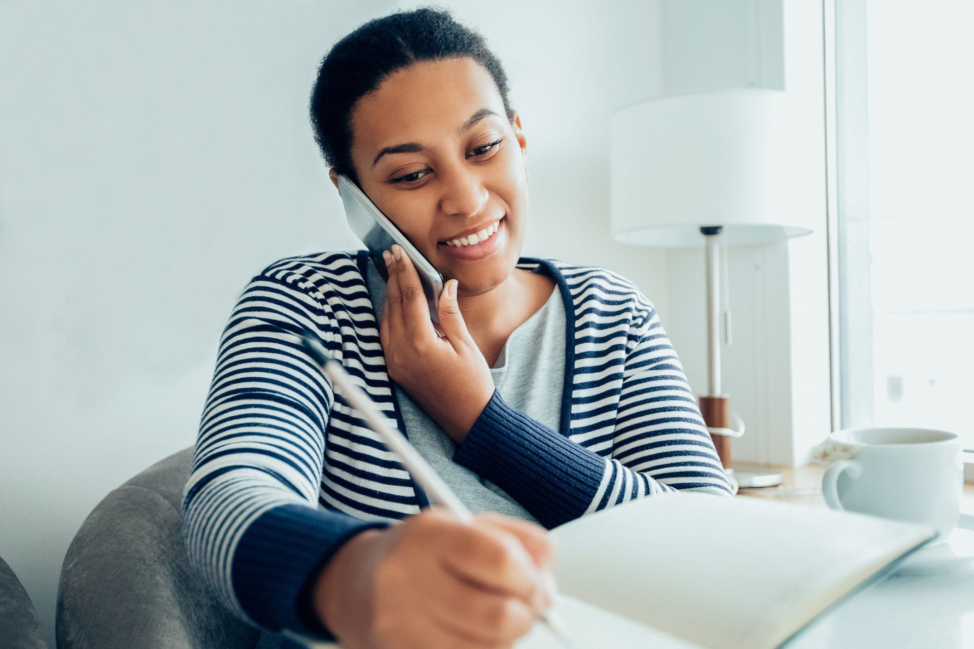 Woman Calling - Olney, Maryland - Star Maids Cleaning Solutions LLC Person smiling while talking on a phone and writing in a notebook on a couch