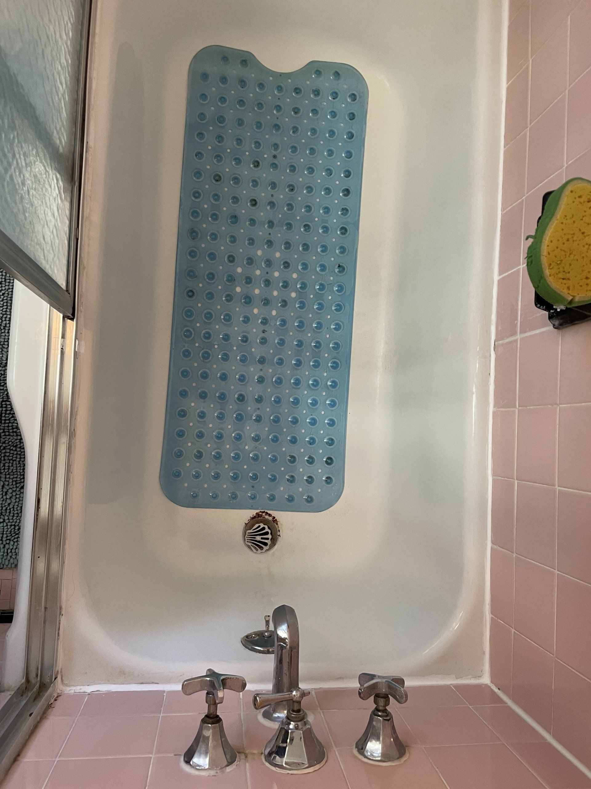 Bathtub with a blue bath mat, chrome faucet, and pink tiled wall.