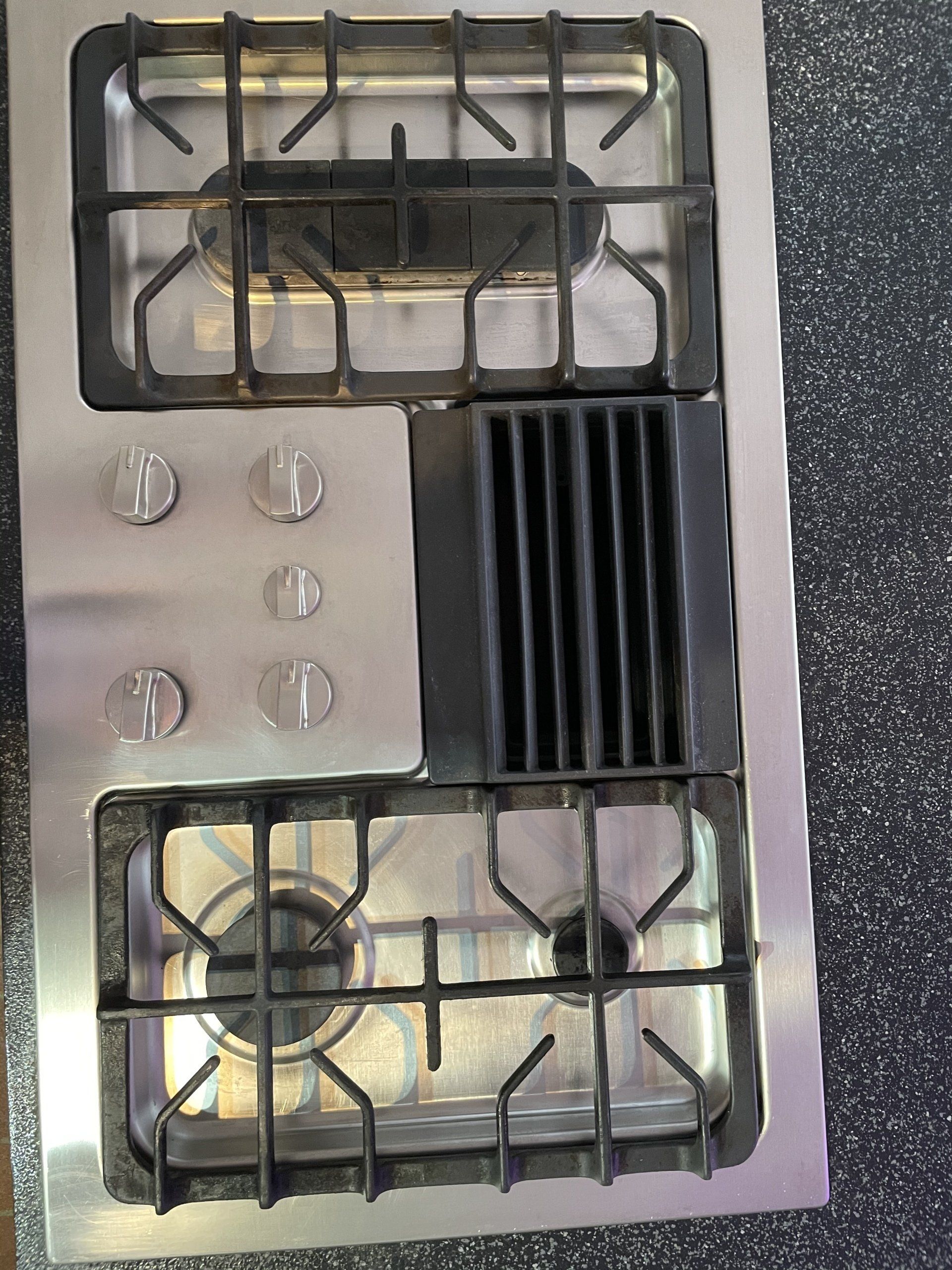 Top-down view of a stainless steel gas stovetop with four burners and black grates.
