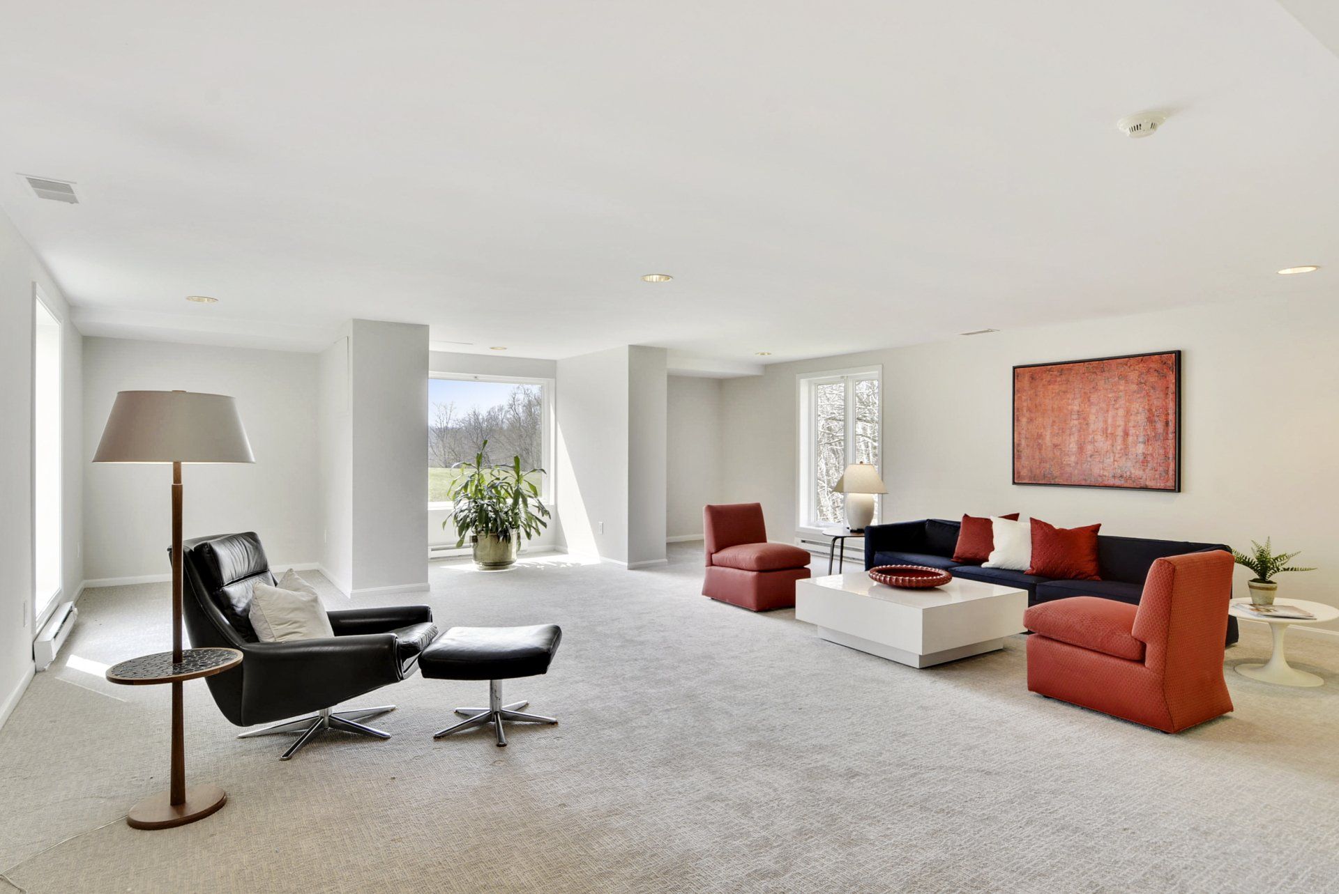 Bright modern living room with white walls, gray carpet, black and red chairs, and a low white coffee table.