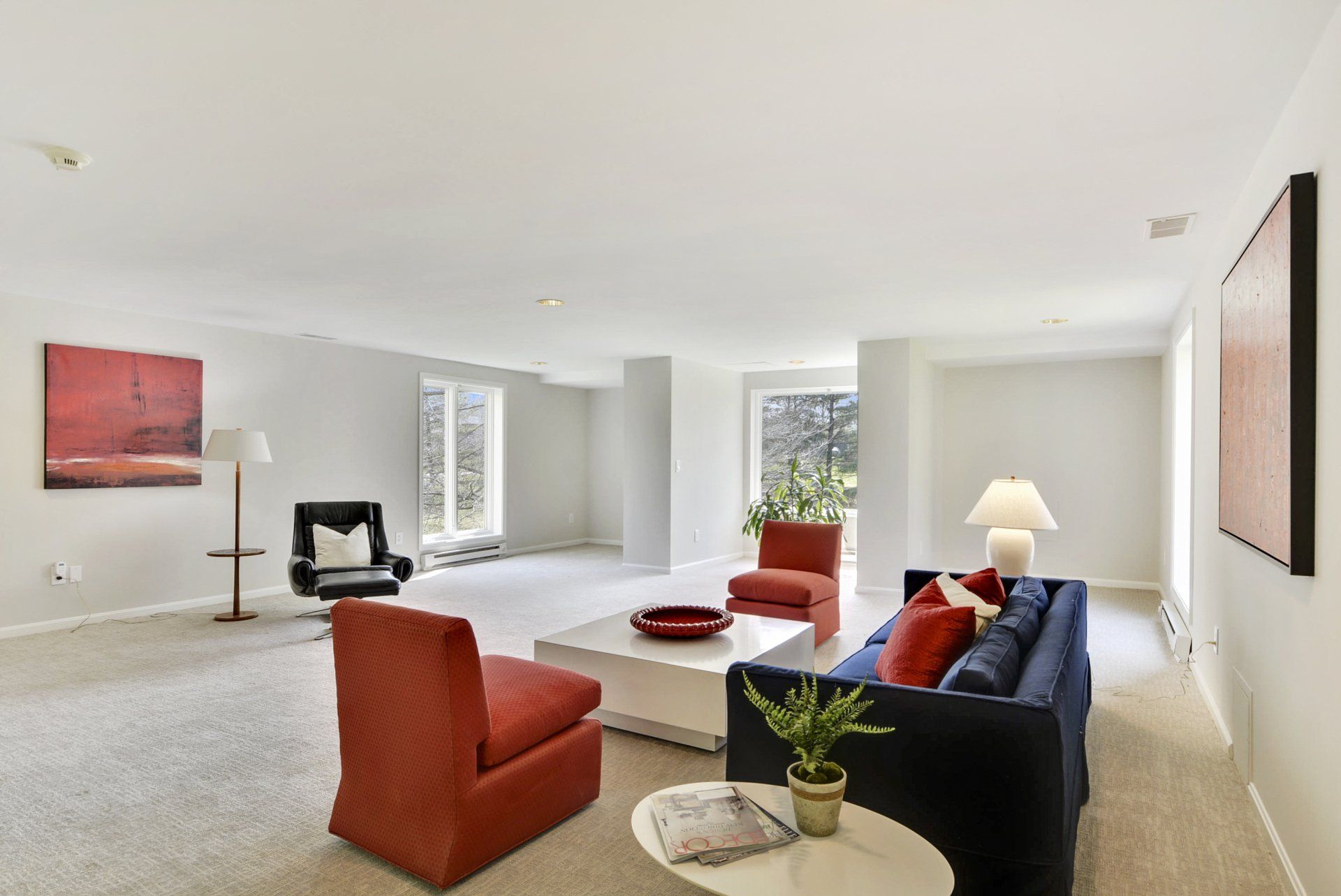 Bright living room with orange chairs, dark blue sofa, white walls, and large windows