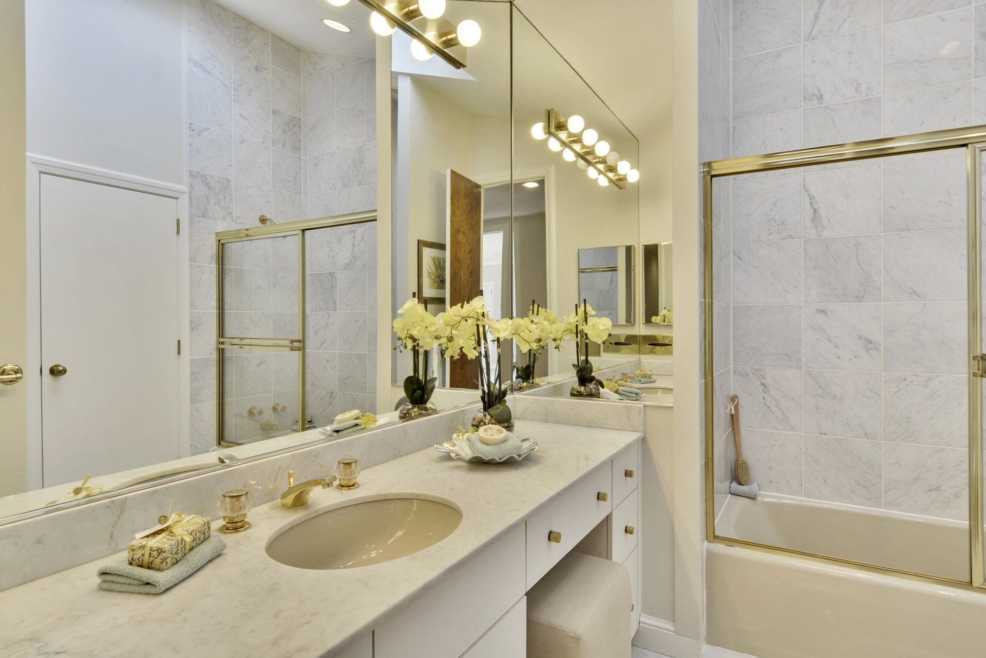 Elegant marble bathroom with gold accents, vanity sink, large mirror, and wall lights