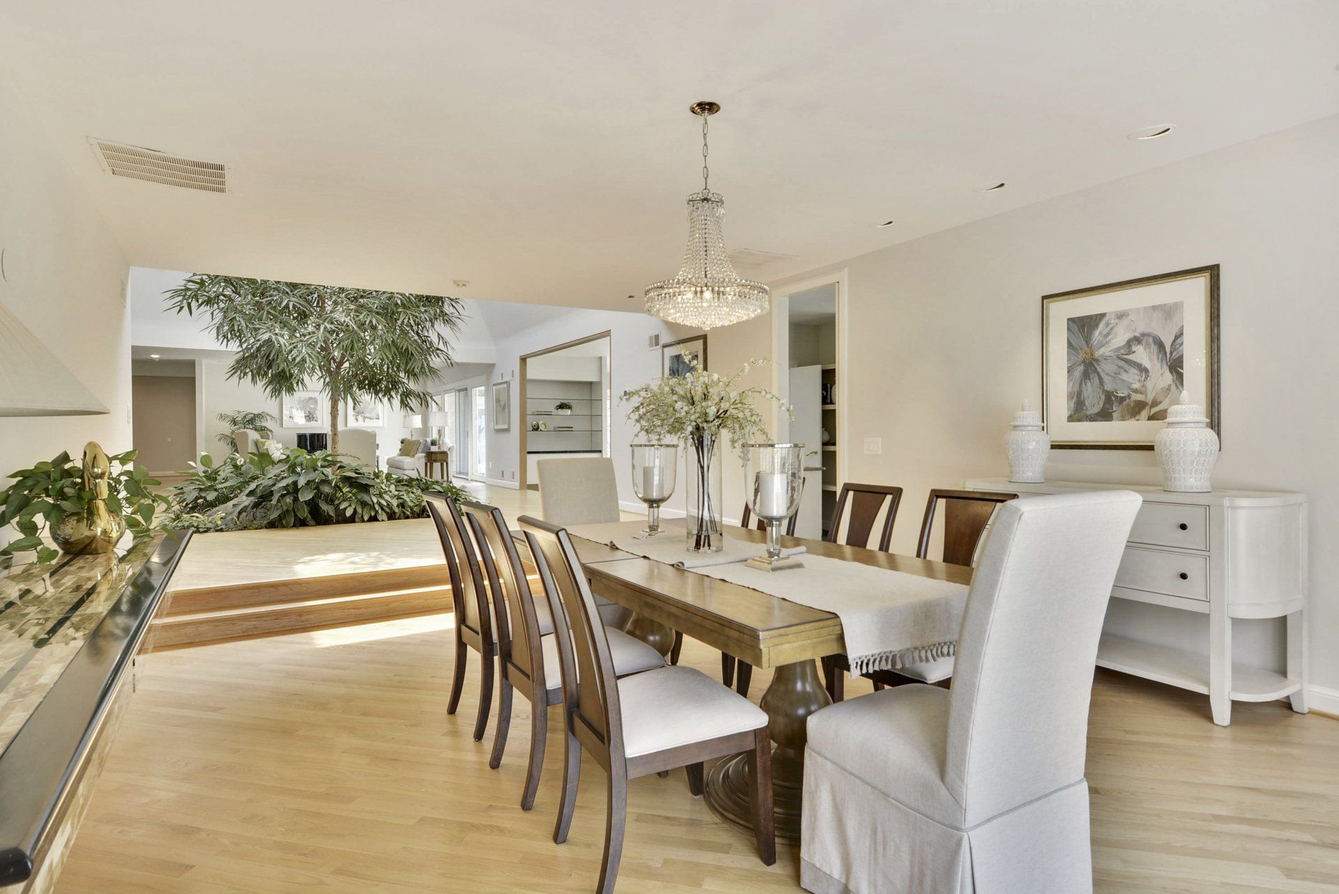 Bright dining room with a long table, white chairs, chandelier, and large mirror.