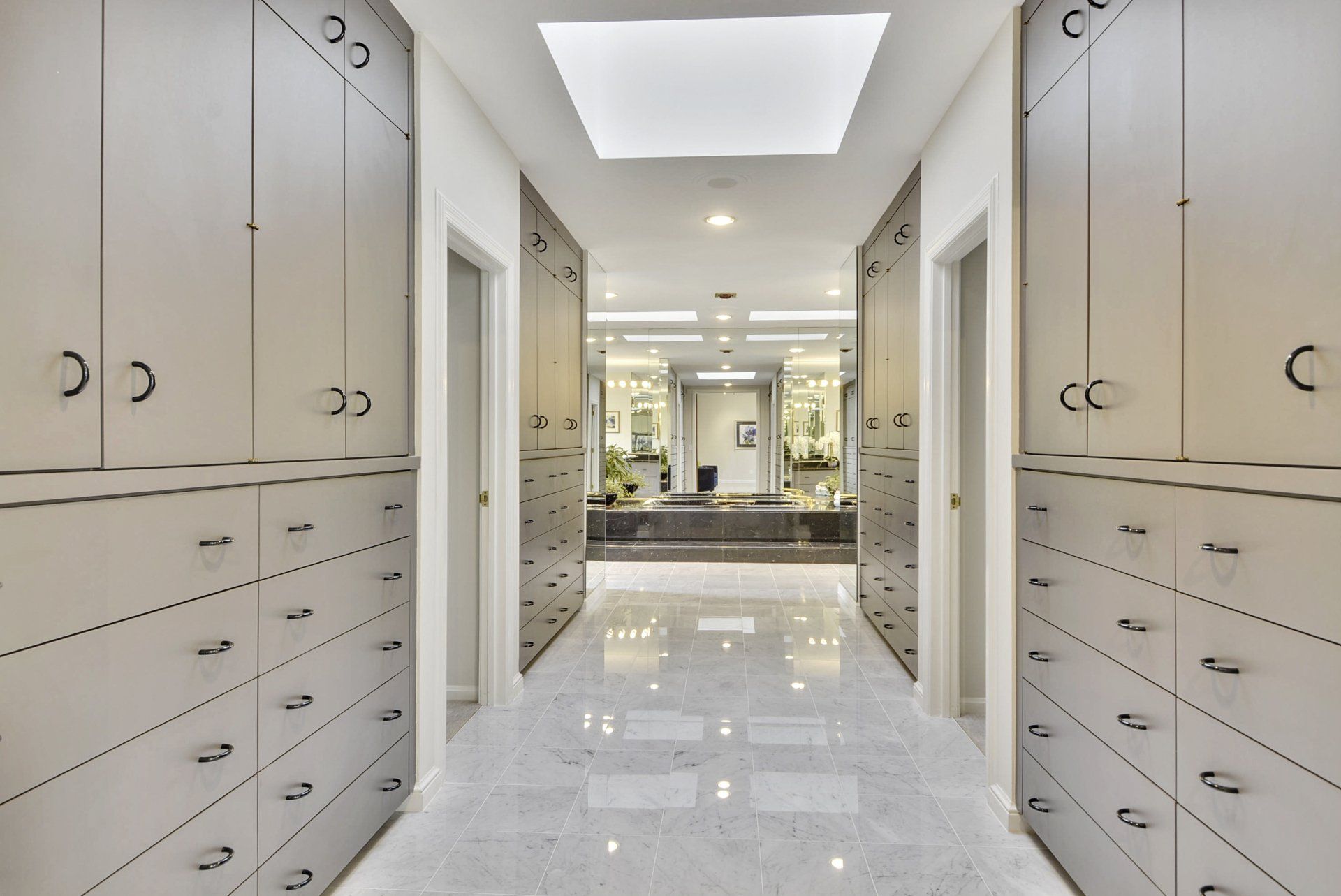 Bright marble walk-in closet with built-in cabinets, drawers, and mirrored vanity at the far end