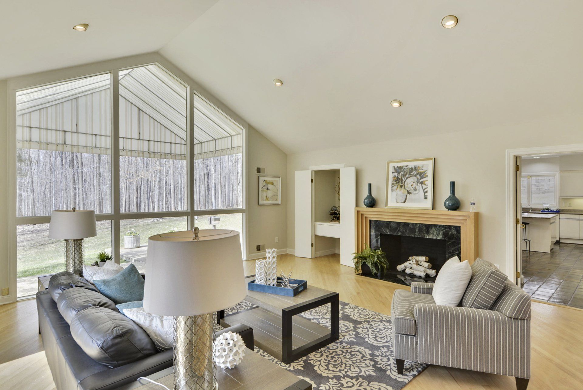 Bright living room with vaulted ceiling, fireplace, large windows, sofa, and patterned armchair