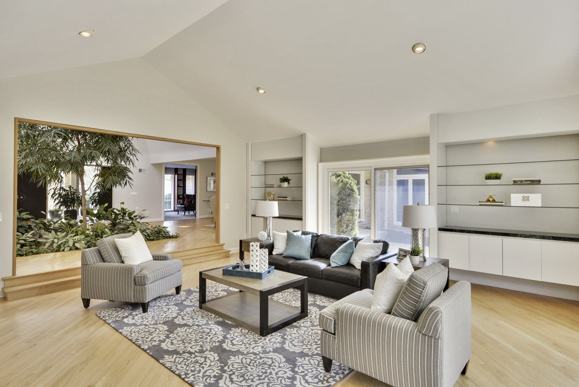 Bright, modern living room with striped armchairs, coffee table, hardwood floors, and large window seat