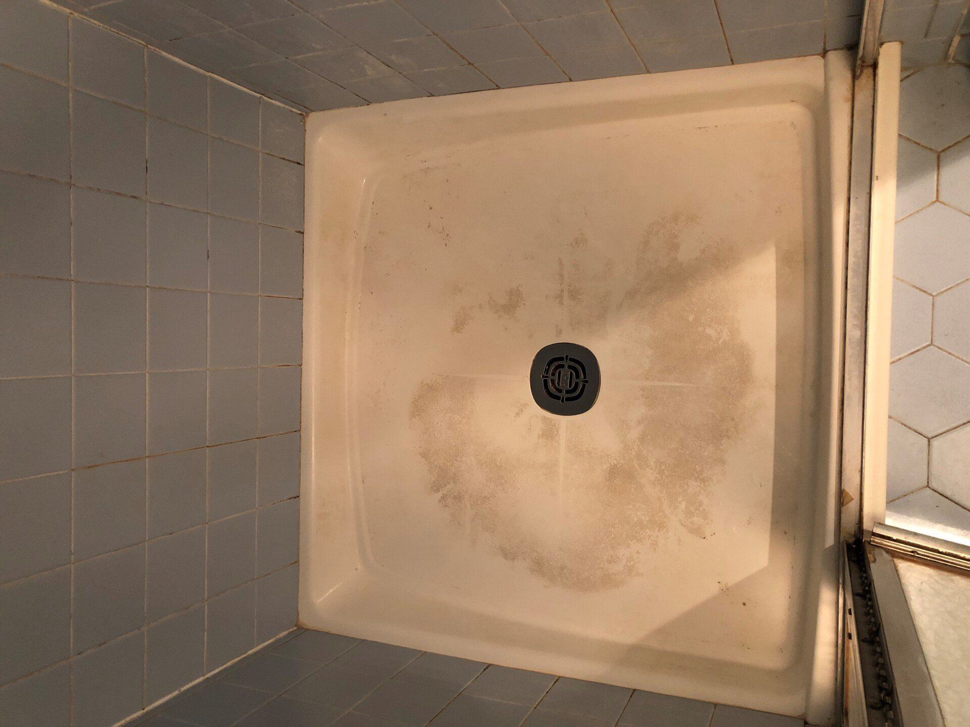 Top-down view of a dirty beige shower stall with a drain in the center.
