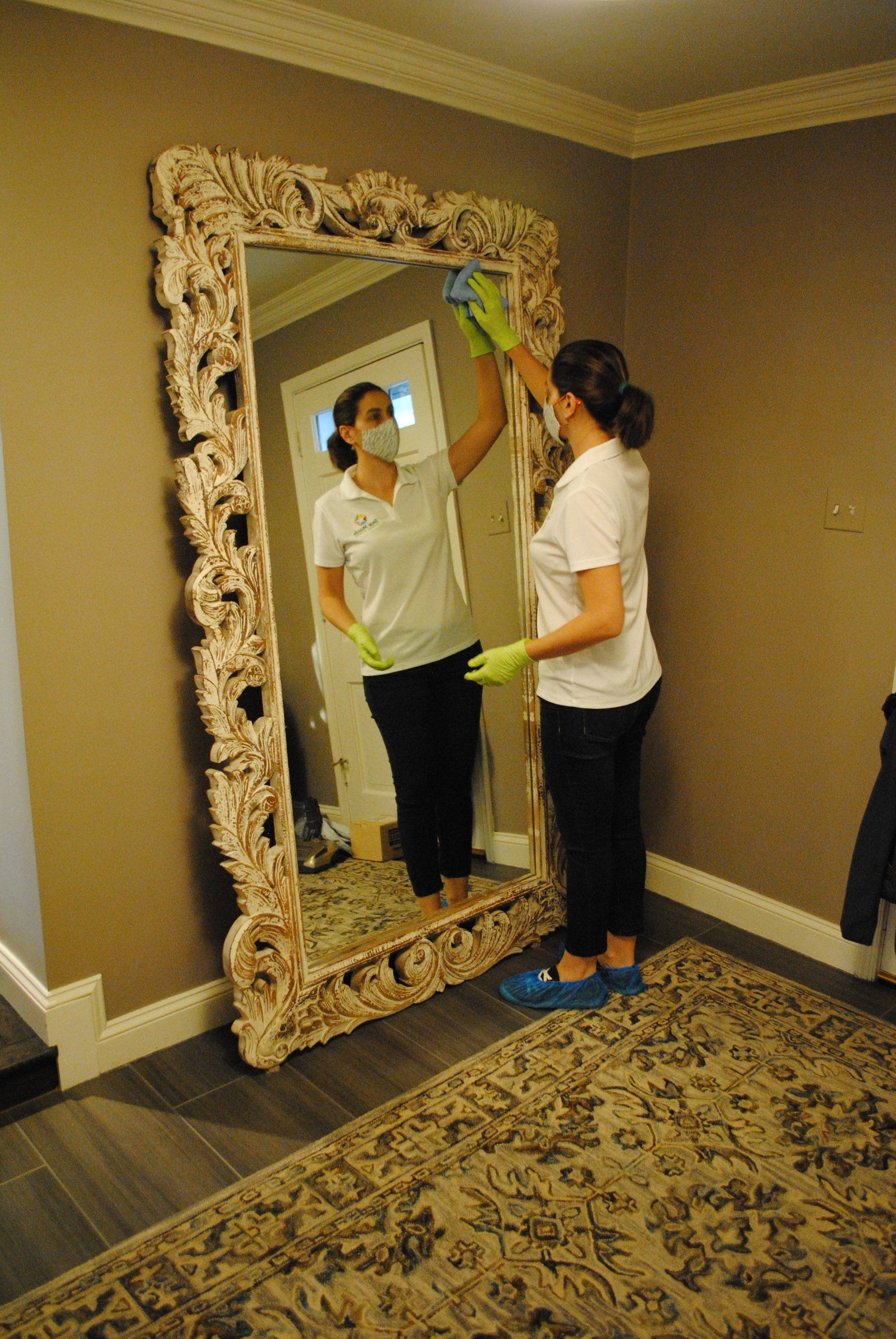 Person standing before an ornate mirror in a beige room, inspecting their reflection.