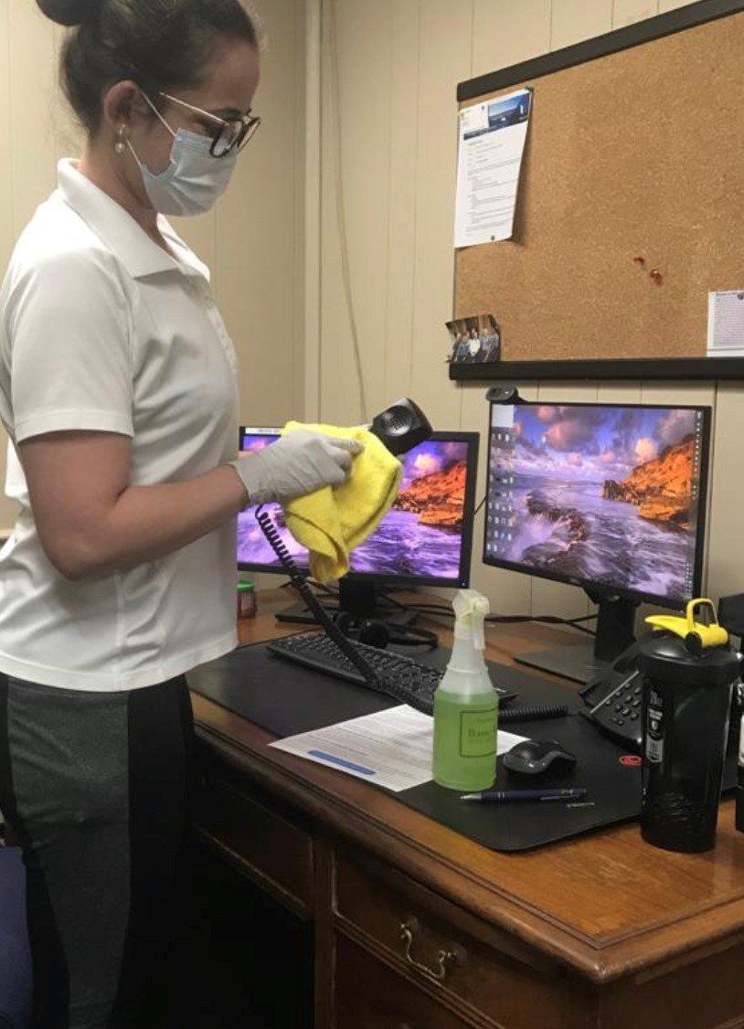 Cleaning Office - Olney, Maryland - Star Maids Cleaning Solutions LLC Person disinfecting dual computer monitors and desk with spray bottle and cloth in an office.