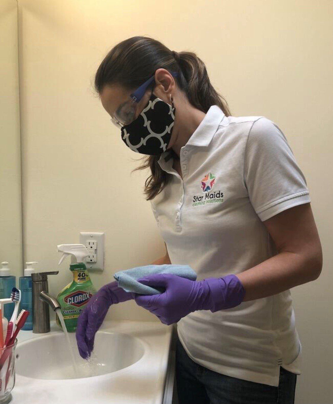 Person wearing gloves and a face mask washing hands at a sink in a clinical setting