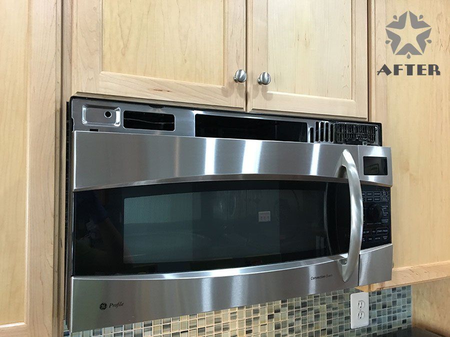 Stainless steel over-the-range microwave above a tiled kitchen countertop and wood cabinets