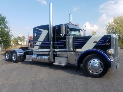Black and white semi-truck with blue accents parked on pavement, under a blue sky.