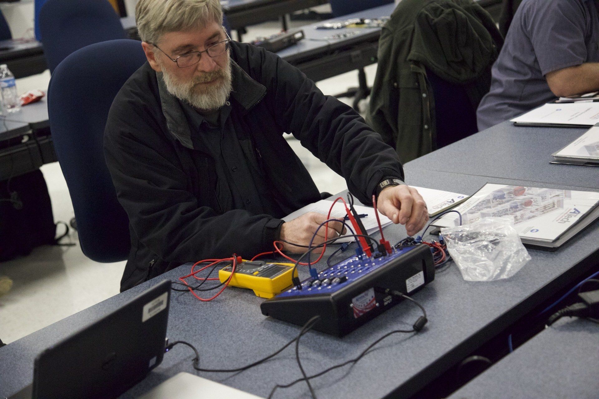 A man with a beard is sitting at a table working on an electronic device.