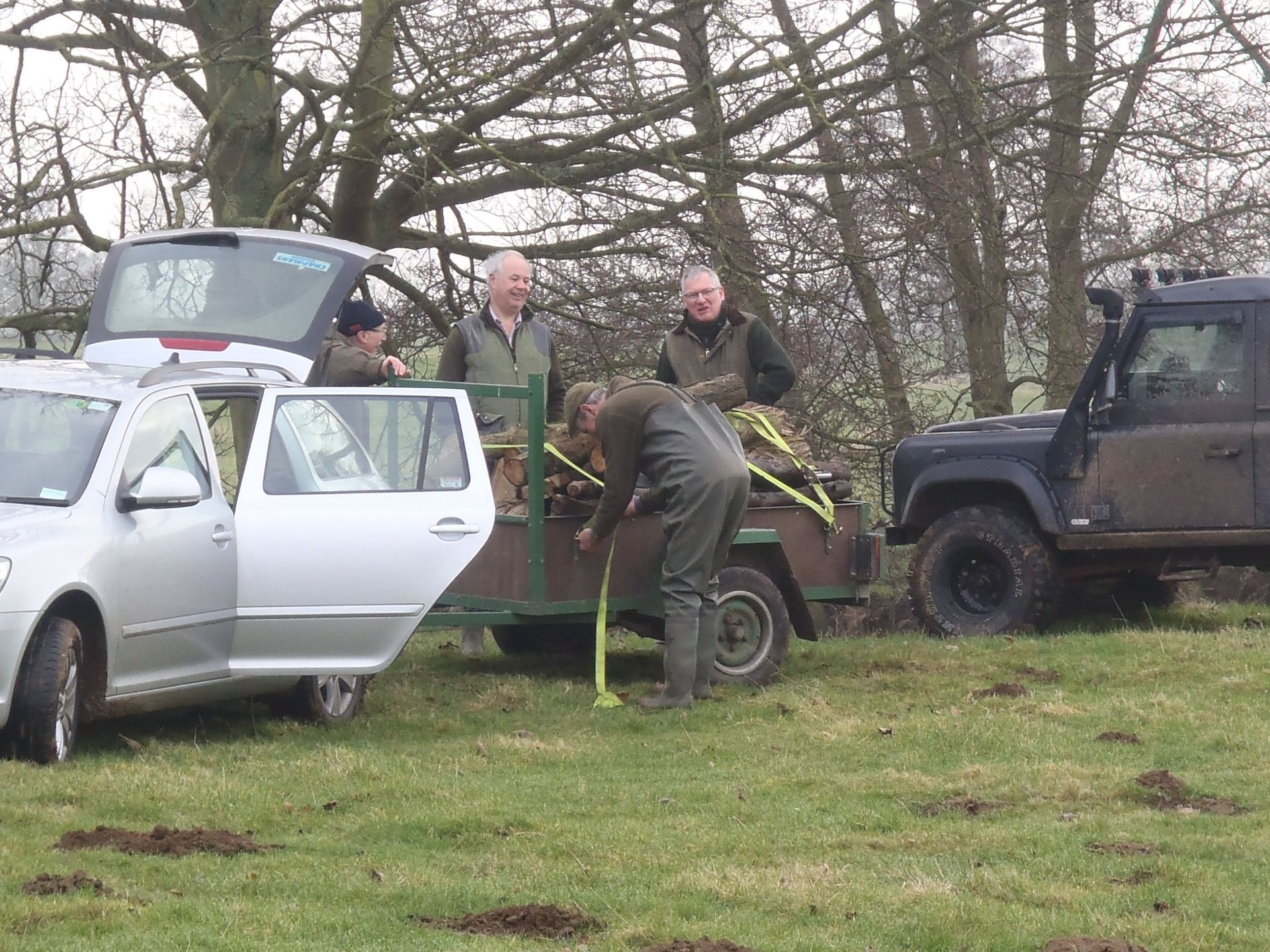 A group of people are standing next to a car in a field.