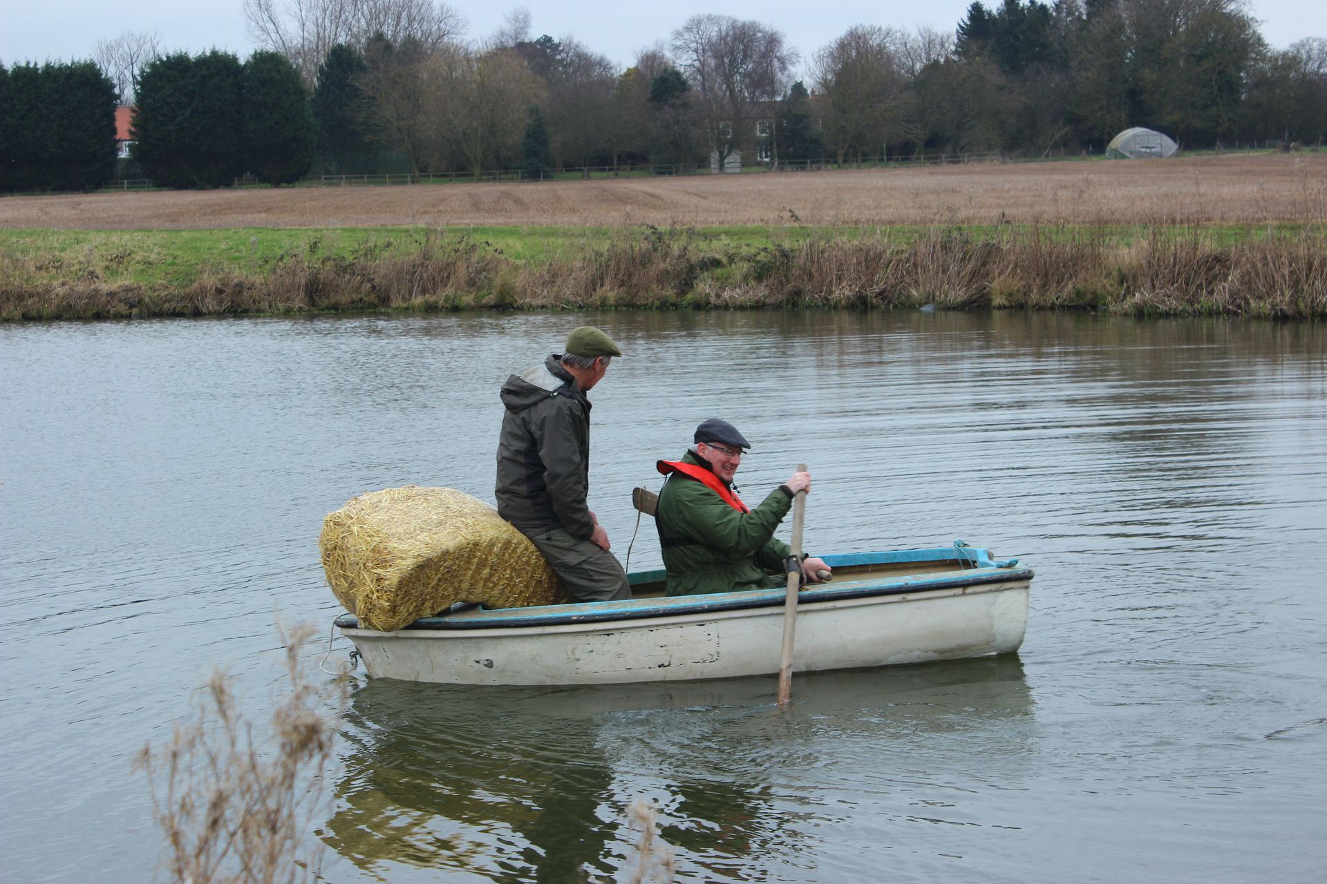 Two men in a boat with a bale of hay on the back
