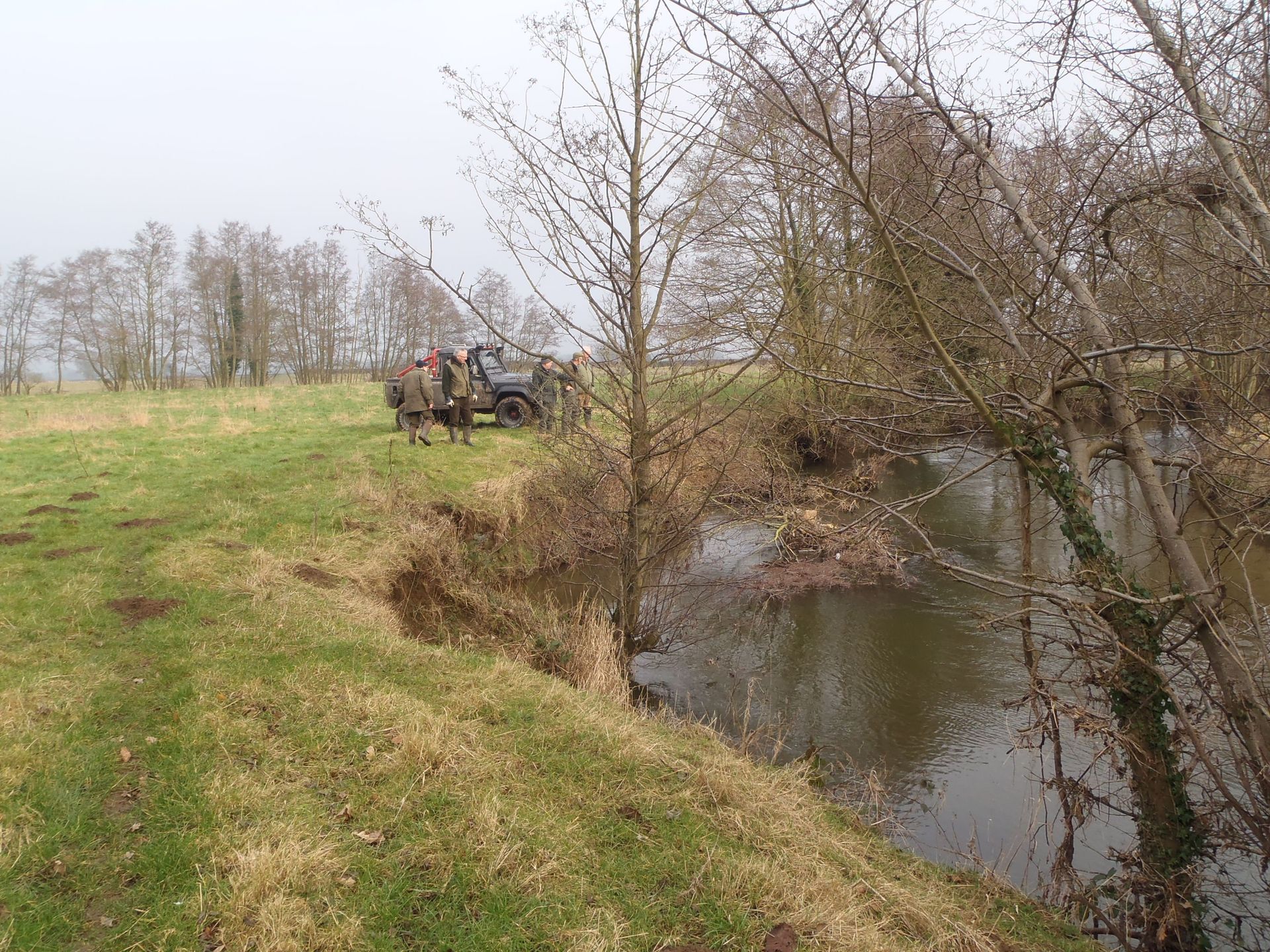 A truck is parked on the side of a grassy field next to a river.