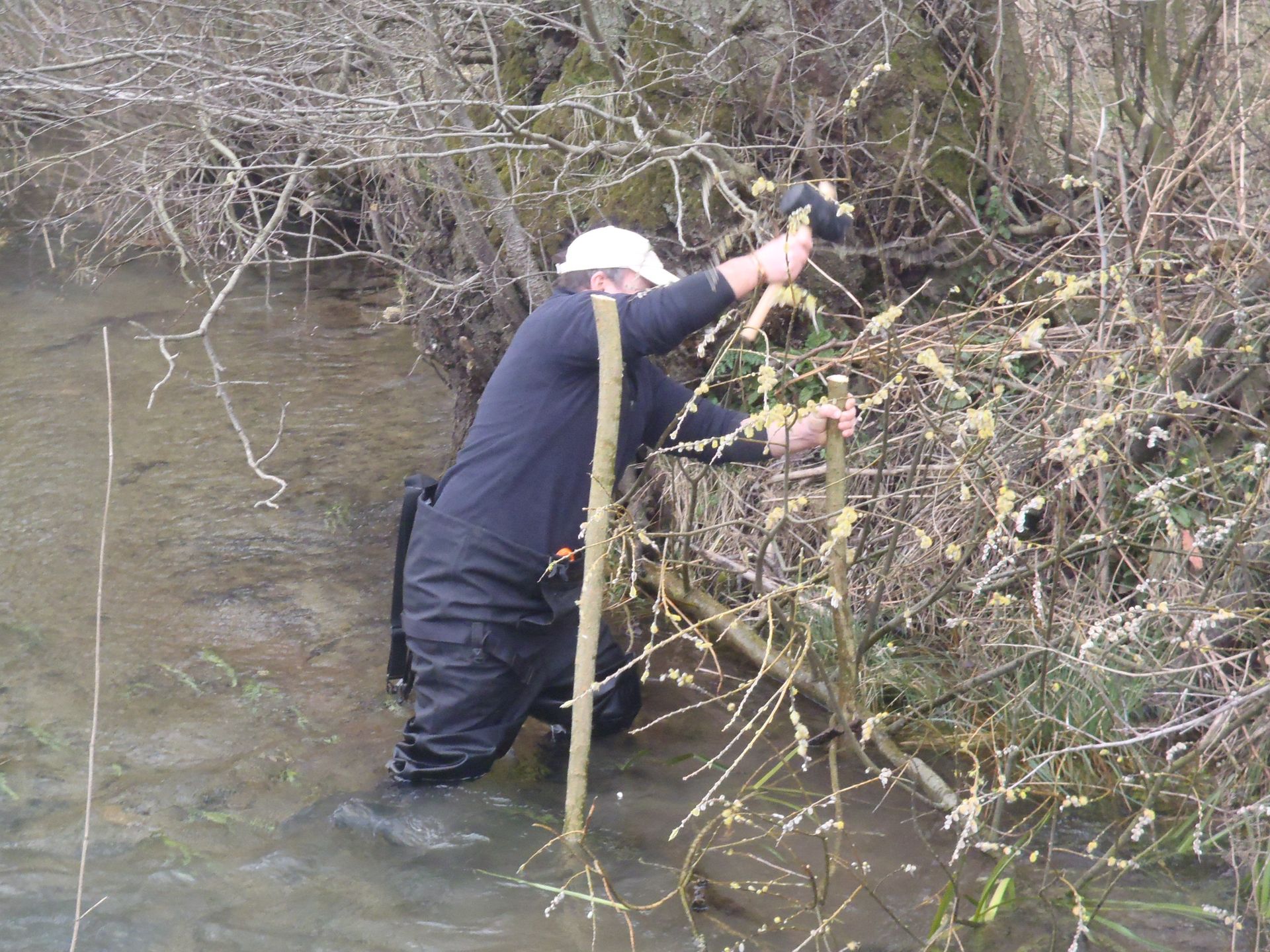 A man is kneeling in the water holding a hammer
