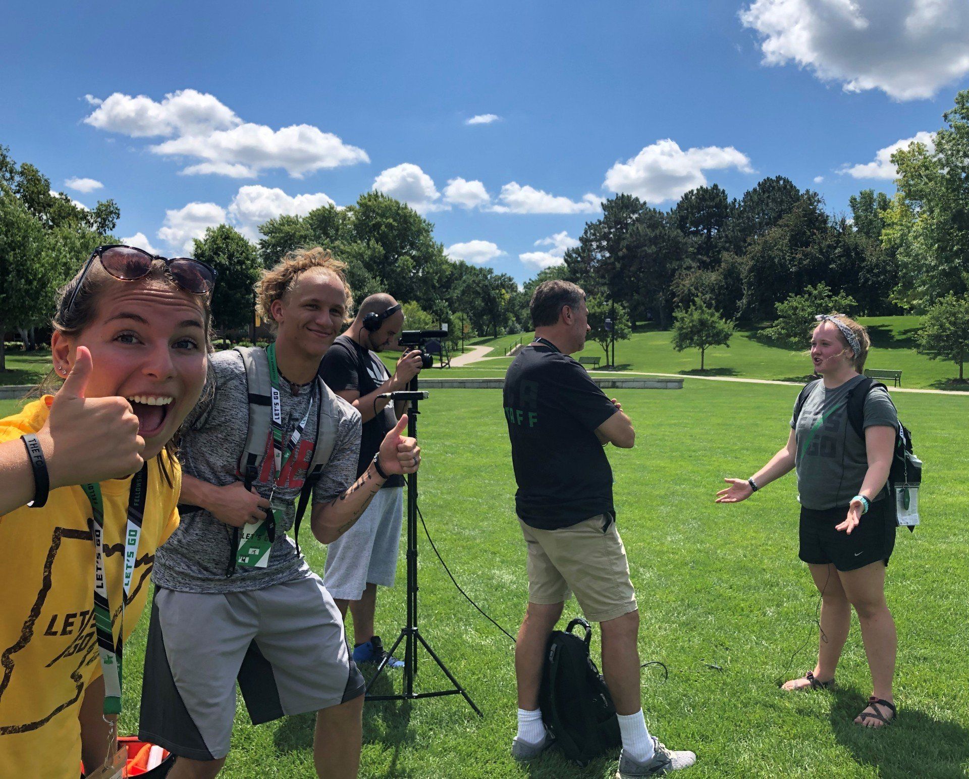 College-age athletes standing on field on a sunny day interviewing in front of video camera.