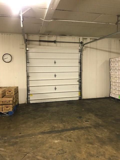 A garage door is open in a warehouse with a clock on the wall.