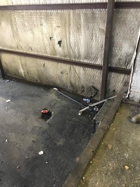 A person is standing next to a wall with a broken piece of metal on the ground.