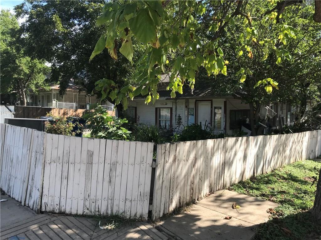 A white wooden fence surrounds a house with trees in the background